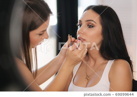 Makeup artist work in her beauty studio. Portrait of Woman applying makeup. Professional make up master. Beautiful make up artist start making a makeup for brunette woman 69899644