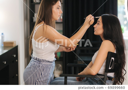 Makeup artist work in her beauty studio. Portrait of Woman applying makeup. Professional make up master. Beautiful make up artist start making a makeup for brunette woman 69899660