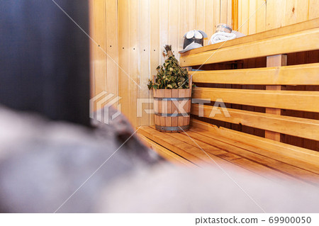 Interior details Finnish sauna steam room with traditional sauna accessories basin birch broom scoop felt hat towel. Traditional old Russian bathhouse SPA Concept. Relax country village bath concept. Interior details Finnish sauna steam room with traditional sauna accessories basin birch broom scoop felt hat towel. Traditional old Russian bathhouse SPA Concept. Relax country village bath concept. 69900050