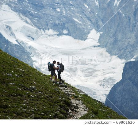 Romantic couple standing on a green meadow at rocky background of Swiss Alps Romantic couple standing on a green meadow at rocky background of Swiss Alps 69901620