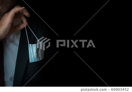 The man takes a disposable medical mask out of his pocket instead of a napkin. A man with a disposable mask in a suit. Respiratory protection. The man takes a disposable medical mask out of his pocket instead of a napkin. A man with a disposable mask in a suit. Respiratory protection. 69903452
