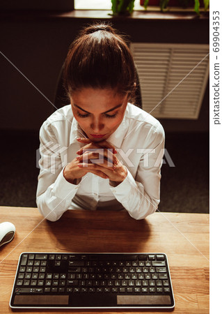 Female office worker sits at her desk with her fingers crossed. Woman looking at computer keyboard on the table. High quality photo 69904353