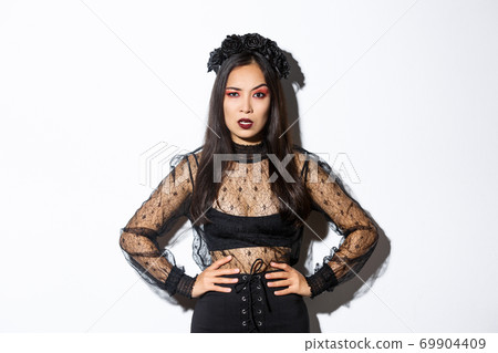 Angry and pissed-off asian female magician, evil witch in black dress and wreath looking mad at someone, frowning and looking judgemental, standing over white background Angry and pissed-off asian female magician, evil witch in black dress and wreath looking mad at someone, frowning and looking judgemental, standing over white background 69904409