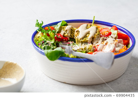 Falafel salad with baked vegetables, tahini dressing and tomatoes in white bowl. Israeli street food concept. 69904435