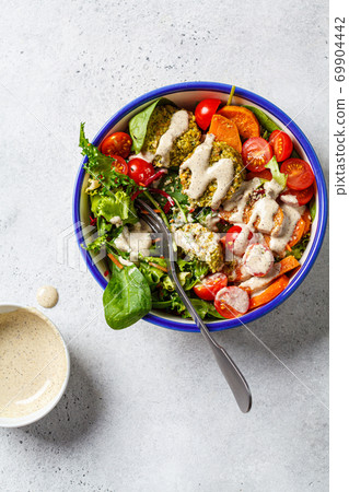 Falafel salad with baked vegetables, tahini dressing and tomatoes in white bowl. Israeli street food concept. Falafel salad with baked vegetables, tahini dressing and tomatoes in white bowl. Israeli street food concept. 69904442