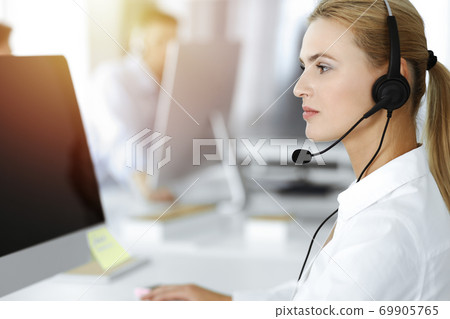 Blond business woman using headset for communication and consulting people at sunny office. Call center Blond business woman using headset for communication and consulting people at sunny office. Call center 69905765
