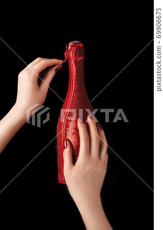Beautiful female hands with trendy red manicure holding champagne bottle in cover spangled with vibrant red sequines on isolated black background. Mockup for your design. Copy space. Flat lay. 69906675