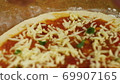 Cooking pizza. Chef put cheese and basil on the base of the pizza greased with tomato paste. A man 69907165