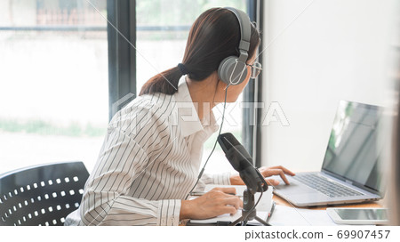 Asian women podcaster podcasting and recording online talk show at studio using headphones, professional microphone and computer laptop on table looking at camera for radio podcast. Asian women podcaster podcasting and recording online talk show at studio using headphones, professional microphone and computer laptop on table looking at camera for radio podcast. 69907457