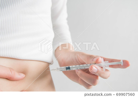 Close up of female diabetes patient making subcutaneous insulin injection into her abdomen with single use syringe at home. Diabetes, insulin dependent, health care and medical concept. Copy space. 69907560