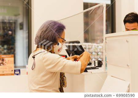 Senior customer wearing protective mask paying money at cashier counter. 69908590