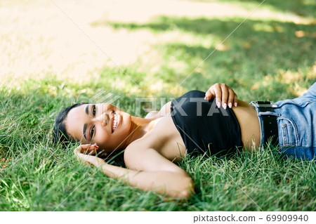 Portrait of pretty happy afro american woman relaxing on grass in park 69909940