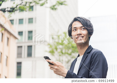 Young man operating a smartphone in the office district Young man operating a smartphone in the office district 69911499
