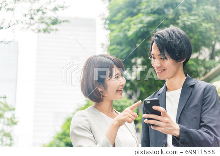 Men and women talking while looking at smartphones in the office district 69911538