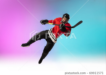 Male hockey player with the stick on ice court and neon colored gradient background. Sportsman wearing equipment, helmet practicing. 69911571