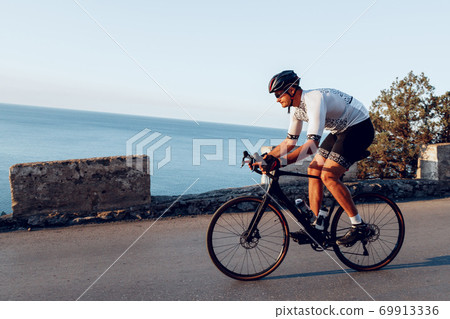 Man cyclist pedaling on a road bike outdoors in sun set 69913336