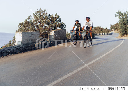 Two professional male cyclists riding their racing bicycles in the morning together Two professional male cyclists riding their racing bicycles in the morning together 69913455
