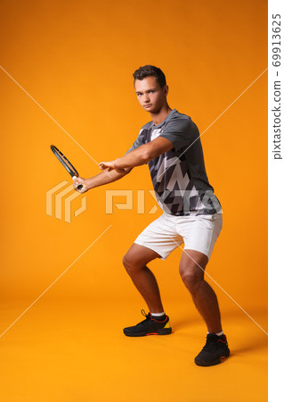 Full-length portrait of a tennis player man in action against orange background 69913625