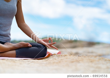A girl is meditating on the rocks at the sea. 69914558