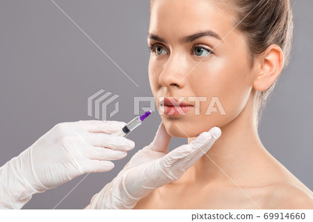 Unrecognizable cosmetitian in gloves injecting lip filler for beautiful lady 69914660