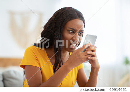 African American woman receiving bad news, angry at her smartphone at home 69914661