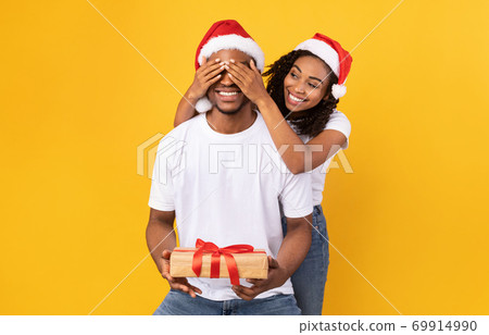 Black Girlfriend Congratulating Boyfriend On Christmas, Covering Eyes, Yellow Background Black Girlfriend Congratulating Boyfriend On Christmas, Covering Eyes, Yellow Background 69914990
