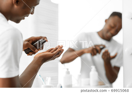 Black Guy Using Aftershave Lotion Standing In Bathroom At Home Black Guy Using Aftershave Lotion Standing In Bathroom At Home 69915068