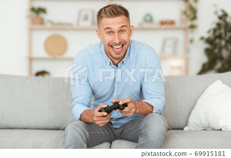 Young guy sitting on couch playing video games 69915181