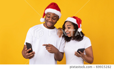 Black Couple Holding Cellphones Recommending Christmas App Over Yellow Background Black Couple Holding Cellphones Recommending Christmas App Over Yellow Background 69915282