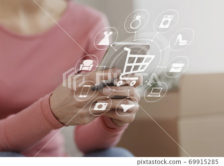 Young lady using mobile phone for online shopping at home, collage with icons of basket trolley and household goods Young lady using mobile phone for online shopping at home, collage with icons of basket trolley and household goods 69915285