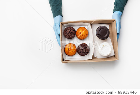 Coffee and sweets of fast food. Waiter in rubber gloves gives order, chocolate muffins and cakes in cardboard box with paper cups takeaway 69915440