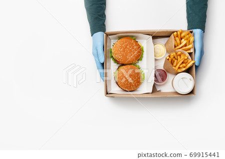 Trendy fast food and lunch for two. Waiter gives box with burger and cheeseburger, french fries in paper packs, with sauce and ketchup, and coffee in cup for client 69915441