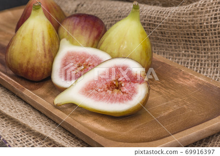 Fresh fig sliced in half with whole figs in the background, on a wooden surface. Fresh fig sliced in half with whole figs in the background, on a wooden surface. 69916397