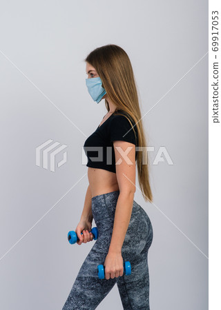 Young woman in a protective mask with dumbbells on a white background. Quarantined sports, covid. 69917053
