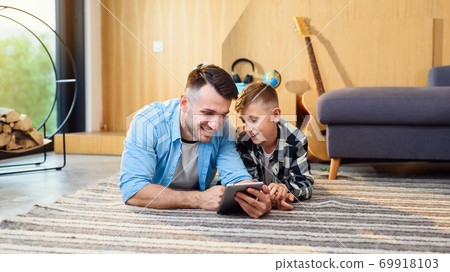 Young boy with father lying on the floor using tablet pc in modern apartment. Happy family time together. 69918103
