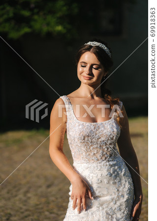 Elegant model in wedding dress posing to photographer outdoors. Beautiful young woman with fashion makeup 69918363