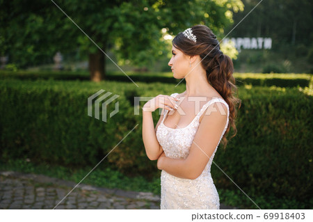 Elegant model in wedding dress posing to photographer outdoors. Beautiful young woman with fashion makeup 69918403