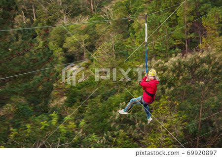 Woman descending by cables in a zip-line on forest Woman descending by cables in a zip-line on forest 69920897