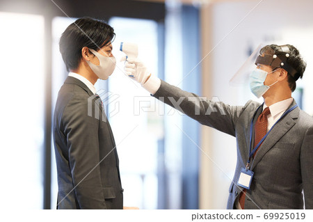 Men taking body temperature measurements with a non-contact thermometer Men taking body temperature measurements with a non-contact thermometer 69925019