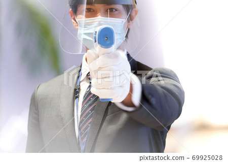 A man in a mask holding a non-contact thermometer A man in a mask holding a non-contact thermometer 69925028