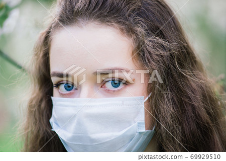 The girl with blue eyes in mask in blossom park. Covid -19 pandemic 69929510