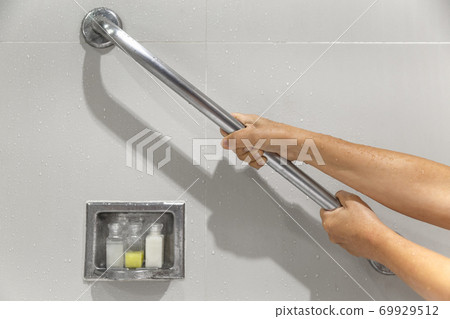 Senior woman holding on handrail for safety in bathroom Senior woman holding on handrail for safety in bathroom 69929512