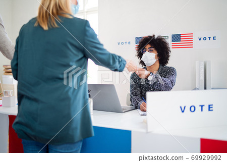 People with face mask voting in polling place, usa elections and coronavirus. 69929992