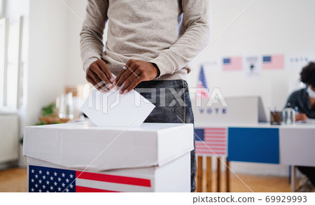 Unrecognizable african-american man putting his vote in the ballot box, usa elections and coronavirus. Unrecognizable african-american man putting his vote in the ballot box, usa elections and coronavirus. 69929993