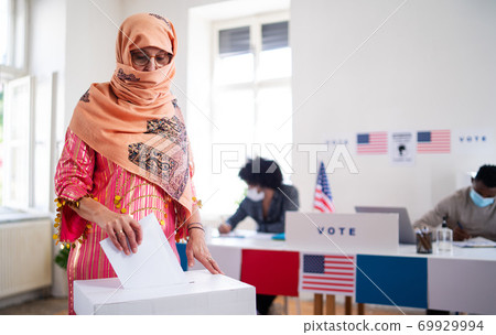 Islamic woman voter putting her vote in the ballot box, usa elections and coronavirus. Islamic woman voter putting her vote in the ballot box, usa elections and coronavirus. 69929994
