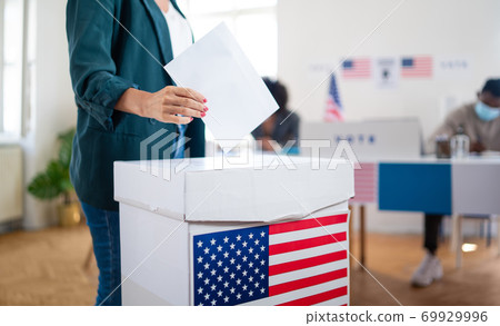 Unrecognizable woman putting her vote in the ballot box, usa and coronavirus elections. 69929996
