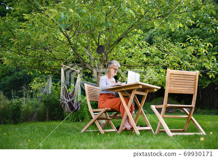 Senior woman with laptop working at the table outdoors in garden, home office concept. 69930171