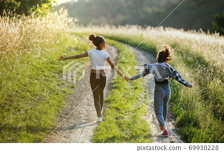 Rear view of young teenager girls friends outdoors in nature, running. 69930228