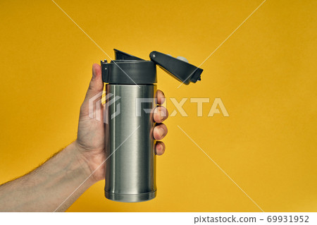 Metal mug thermos in hand on a colored background. Hot drinks on the go. Thermo mug. Metal mug thermos in hand on a colored background. Hot drinks on the go. Thermo mug. 69931952