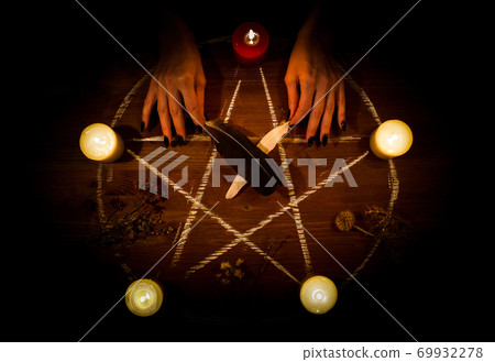 Female hands on the altar in the dark. Witch does magic using pentagram, candles, feathers, dry herbs on wooden surface, selected focus, low key. 69932278